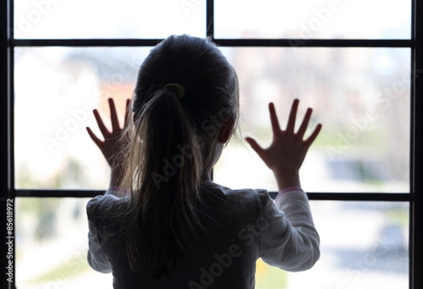 Fototapeta Young girl at window (in partial silhouette) hands pressed against window, pensive or wanting out?