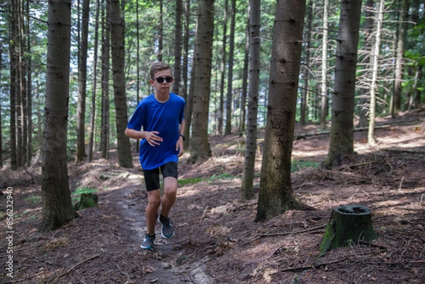 Fototapeta A young man runs along a path in the forest.