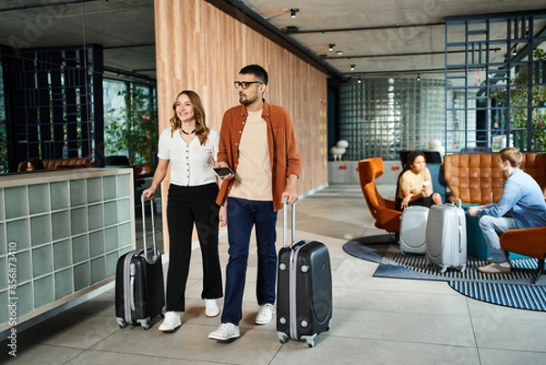 Obraz A man and a woman, colleagues, stand with their luggage in a hotel lobby during a corporate trip.