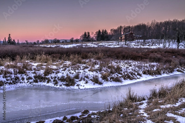 Fototapeta Zamarznięty strumień w środku zimy o wschodzie słońca ze śniegiem w polu