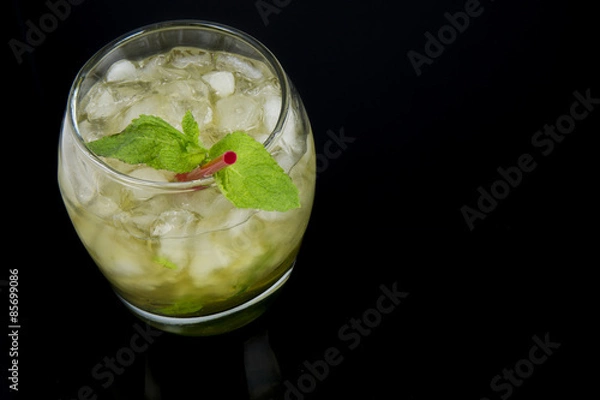 Fototapeta A Mint Julep, the official drink of the Kentucky Derby, with fresh mint leaves, crushed ice, and a red stir stick with a black background. Drink is oriented on the left side of the photo.