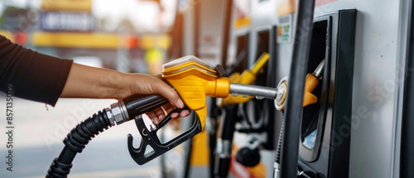 Fototapeta Hand operating a fuel pump at a gas station, highlighting the process of refueling a vehicle with a modern pump handle amidst a busy station backdrop.