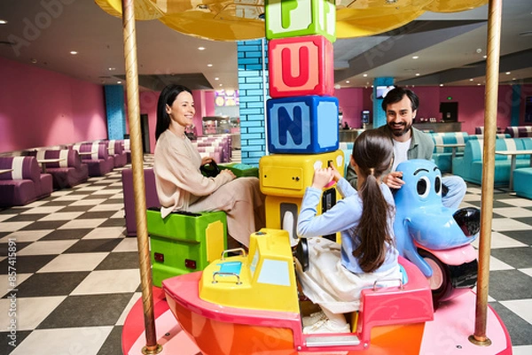 Fototapeta A joyful family spins on a carousel in a vibrant toy store, laughter filling the air during a weekend outing at the malls gaming zone.