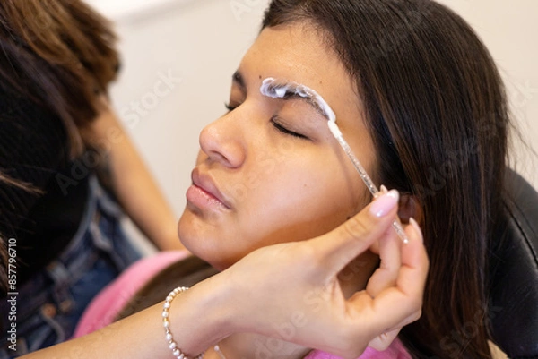 Fototapeta Beautician making eyebrow design and lamination procedure. Young latin woman in a professional beauty salon for threading and brow shape correction