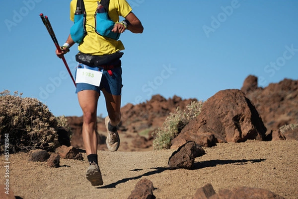 Fototapeta Trail running runner man on endurance run with hydratation trail vest on volcano mountain. Ultra marathon race athlete on volcanic rocks path in mountains landscape