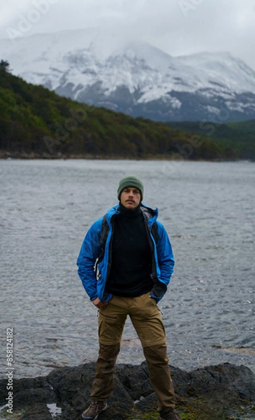 Obraz Photo of a handsome young man with mustache, wearing a green woolly hat and blue jacket, posing in front of the Beagle Channel in Tierra del Fuego National Park, Argentina.