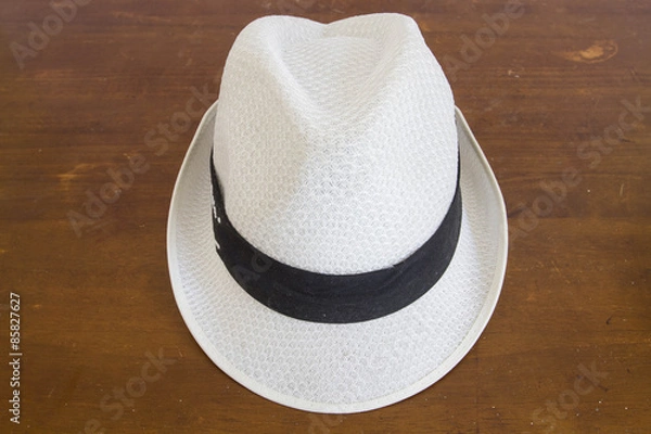 Fototapeta White hat with a hatband on a wooden table against dark background