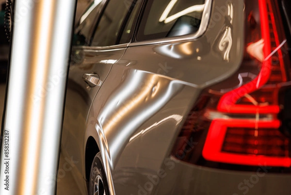 Fototapeta A silver car with a red brake light is parked in a garage with hail damage problems