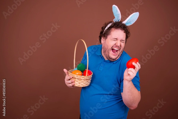 Obraz Happy holidays. Funny fat man in an Easter bunny costume. Brown background.