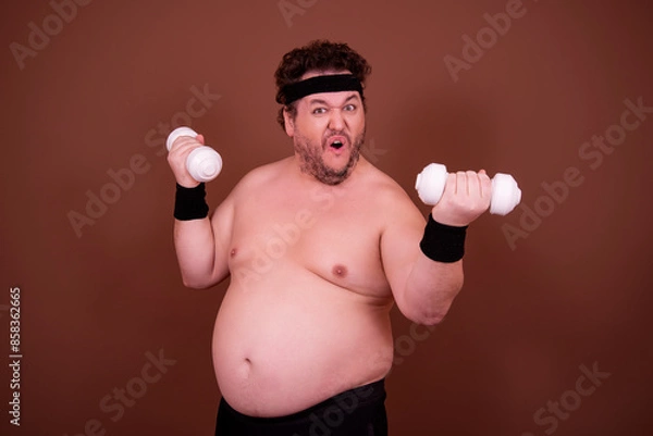 Fototapeta Fitness and healthy lifestyle. A funny fat man is doing sports. Brown background.