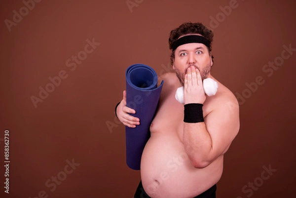 Obraz Fitness and healthy lifestyle. A funny fat man is doing sports. Brown background.