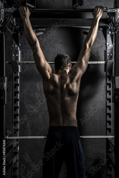 Fototapeta Bodybuilding, Young Athletic Strong Man showing Back Muscles working on Fitness Bar, Strong Contrast with Desaturated Grunge filter