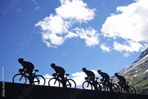 Fototapeta Lanslebourg-Mont-Cenis , France - June 20 2024: A group of cyclists tackle the steep Alpine climb in the back light.