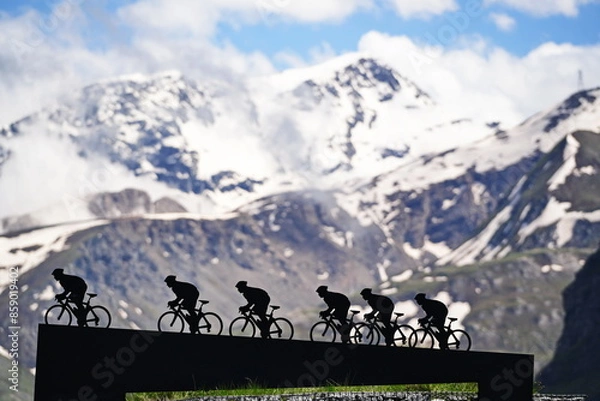 Fototapeta Lanslebourg-Mont-Cenis , France - June 20 2024: A group of cyclists tackle the steep Alpine climb in the back light.