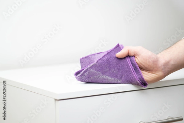 Fototapeta close up of a male hand wiping dust with microfiber towel cloth on white surface wardrobe, dust visible on the towel, copy space cleaning dust, A hand using a cloth to clean the dust