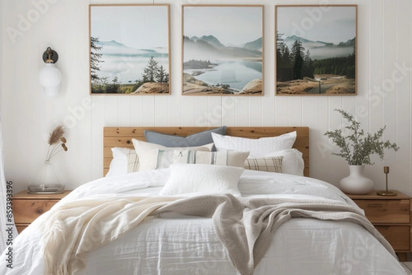 Fototapeta A tranquil white bedroom with a wooden bed frame, soft linens, and calming landscape posters above the bed.