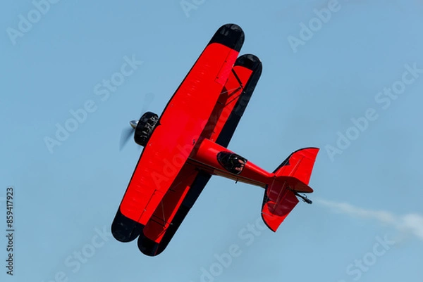 Fototapeta Red bi-plane flying stunts during an airshow with smoke on. This plane has a powerful radial engine and a closed cockpit. It is flying in a knife edge manuver.