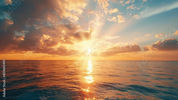Fototapeta The sun sets over a calm sea, casting warm light on the water. Clouds scatter across the sky, creating a beautiful, peaceful scene.