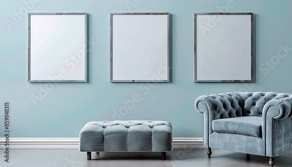 Fototapeta Three square frames on a pale blue wall in a living room. The room features a gray velvet armchair and a matching blue ottoman.