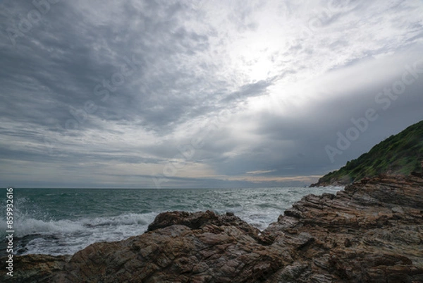 Fototapeta Waves crash against a rocky shoreline with mountains in the background