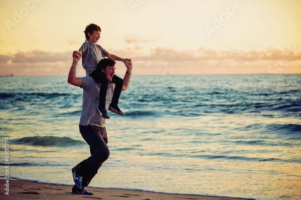 Fototapeta Happy father and son having great time on the beach in sunset