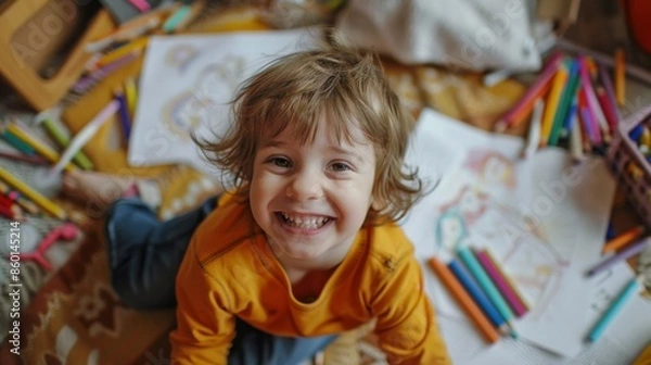 Fototapeta A child with a messy coloring area, crayons and papers scattered everywhere, but with a big smile
