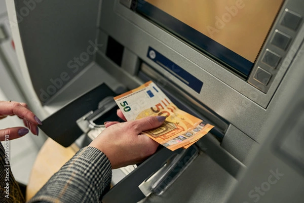 Obraz Zooming in on the moment, the woman confidently retrieves crisp bills from the ATM, completing a seamless and secure financial transaction.