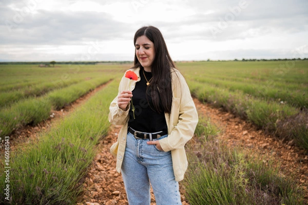Fototapeta Young woman with red poppy and pretty smile in a lavender field