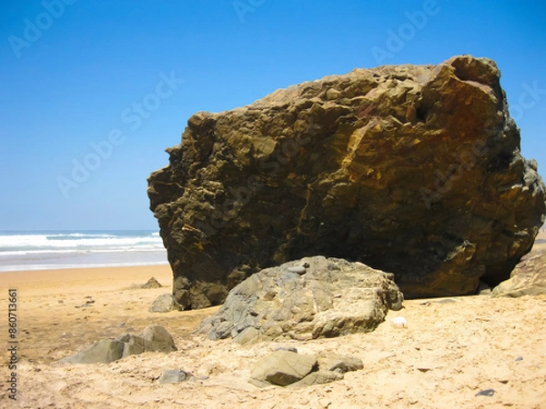 Fototapeta A large rock is positioned on a sandy coastline by the sea