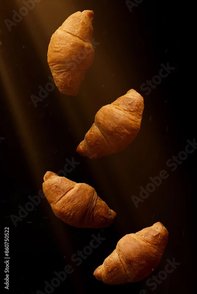 Fototapeta Several croissants on a black background illuminated by rays