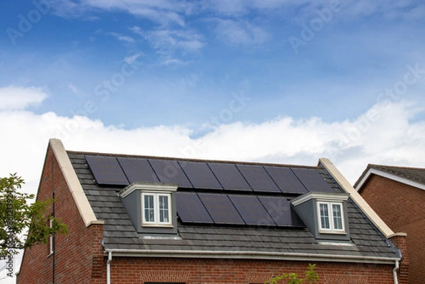Fototapeta Photo of a modern British house in the UK with electrical solar panels on the roof on a bright sunny day with clouds in the sky