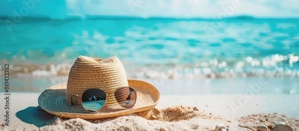 Fototapeta Beach essentials like a summer hat and sunglasses arranged neatly on the sand with a picturesque view of the ocean, inviting you to relax. image with copy space