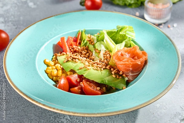 Fototapeta Avocado salad bowl with smoked salmon and fresh vegetables on a sunlit textured surface