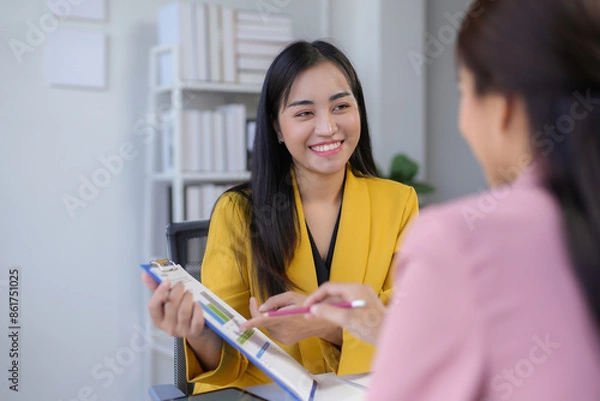 Obraz Smiling asian businesswoman showing charts and explaining results to colleague