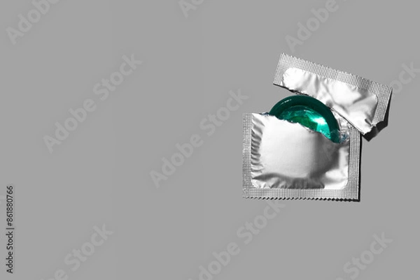 Fototapeta Condom half out of package on a grey background. A condom use to reduce the probability of pregnancy or sexually transmitted disease (STD). Safe sex and reproductive health concept. Top view.