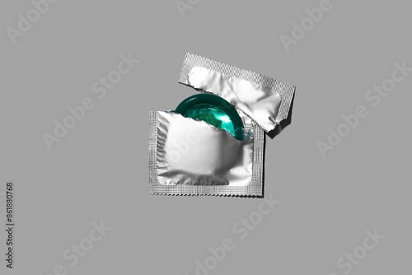 Fototapeta Condom half out of package on a grey background. A condom use to reduce the probability of pregnancy or sexually transmitted disease (STD). Safe sex and reproductive health concept. Top view.