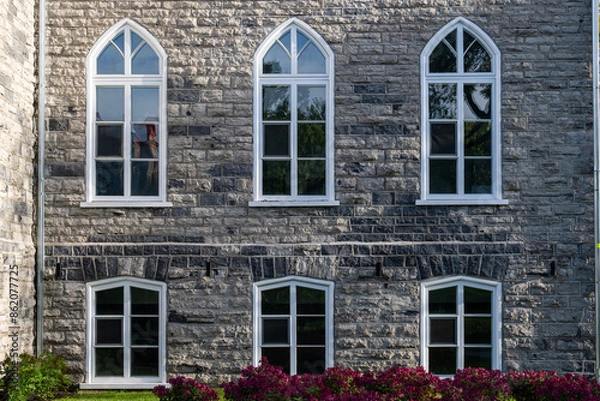 Fototapeta A historical concrete building, Gothic Revival style of architecture with multiple windows. Clean mason style with grey and beige bricks on the frame and six clerestory cathedral glass windows.