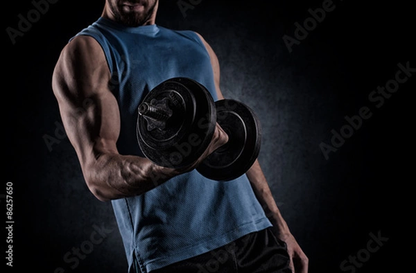 Fototapeta young man with dumbbell flexing muscles over gray background