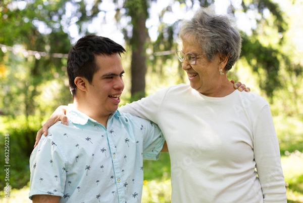 Obraz A young man and an older woman smile and embrace in a park. The man is wearing a blue shirt with palm trees. The scene is joyful and comforting.