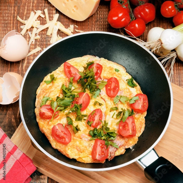 Fototapeta Omelette with ham, tomatoes and chees on the frying pan.