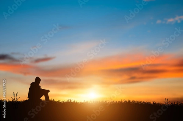 Fototapeta Silhouette of young man sits and praying alone at the top of the mountain at sunset with beautiful natural sunlight.