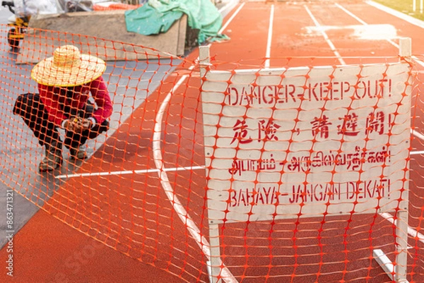 Fototapeta Danger Keep Out signage in multiple language on running track with worker repair in construction site