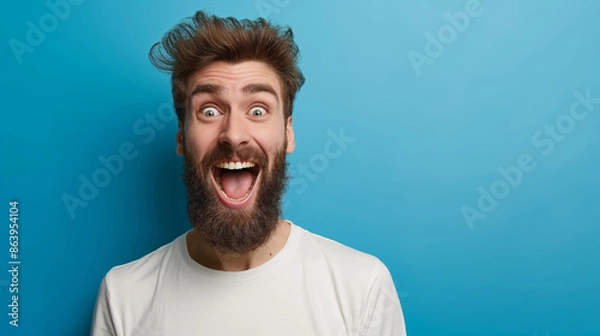 Fototapeta A man with a beard and a white shirt is smiling and laughing. He has a big smile on his face and his eyes are wide open. Concept of happiness and joy