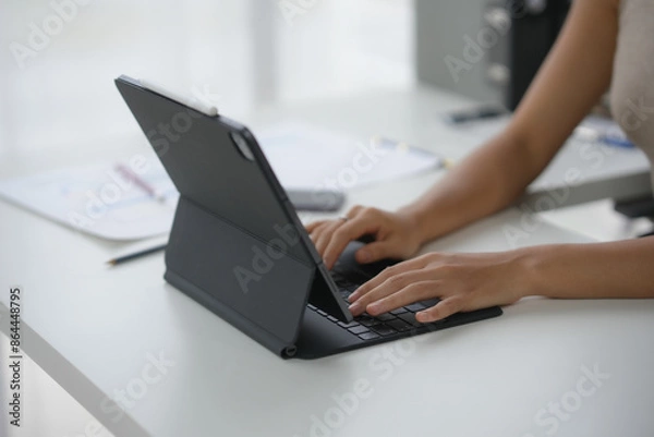 Fototapeta A person working on a tablet with a keyboard in an office setting, focusing on productivity and technology use. Modern workspace with natural light.