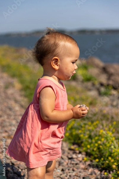 Fototapeta Toddler girl picking up rocks from in front of ocean 