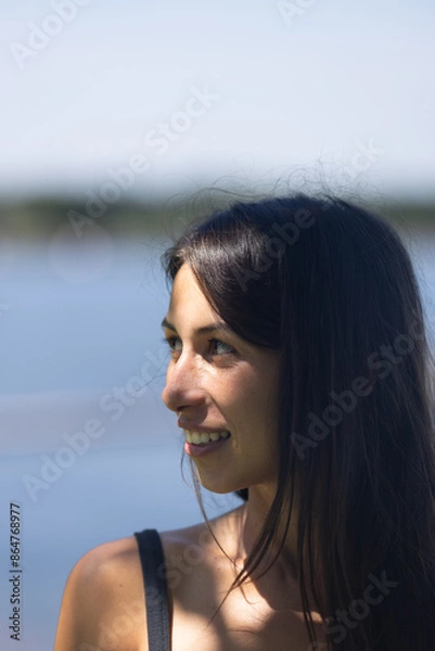Fototapeta Woman in 20s smiling and looking happy in front of ocean 