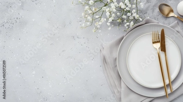 Obraz A simple table setting featuring two gold forks, a knife, and a spoon on a white napkin, with two white plates on a grey surface