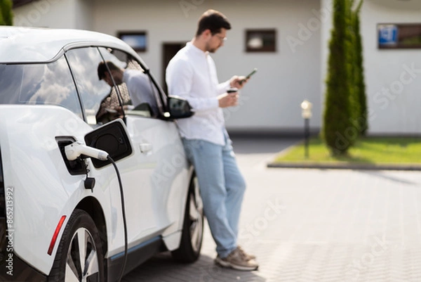 Obraz Man Charging Electric Car While Using Smartphone Outdoors