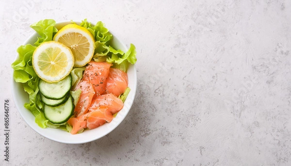Fototapeta Bowl of salted salmon with fresh lettuce, cucumbers and lemon slices. Ketogenic-friendly lunch.