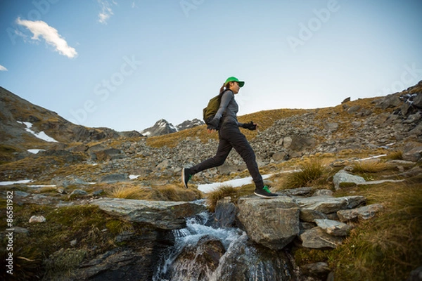 Fototapeta Female hiker leaping across a stream